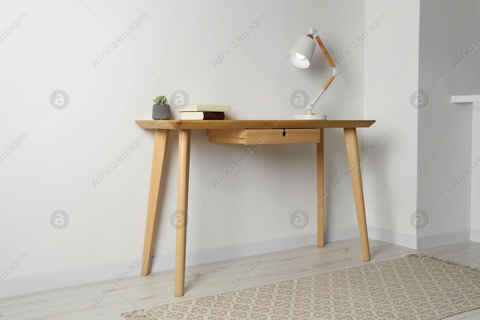 Photo of Stylish lamp, books and houseplant on wooden table in light room. Interior design