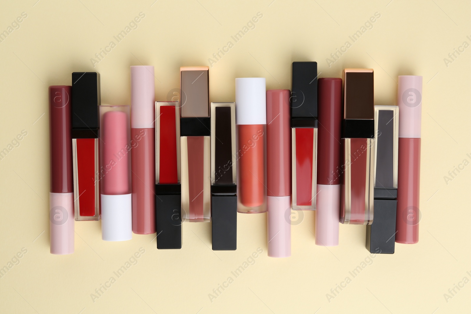 Photo of Different lip glosses on pale yellow background, flat lay