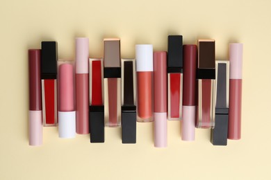 Different lip glosses on pale yellow background, flat lay