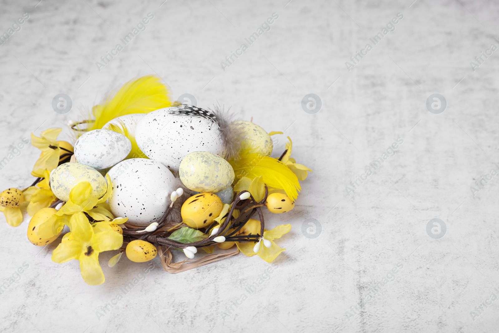 Photo of Decorative nest with many painted Easter eggs on light textured background, space for text