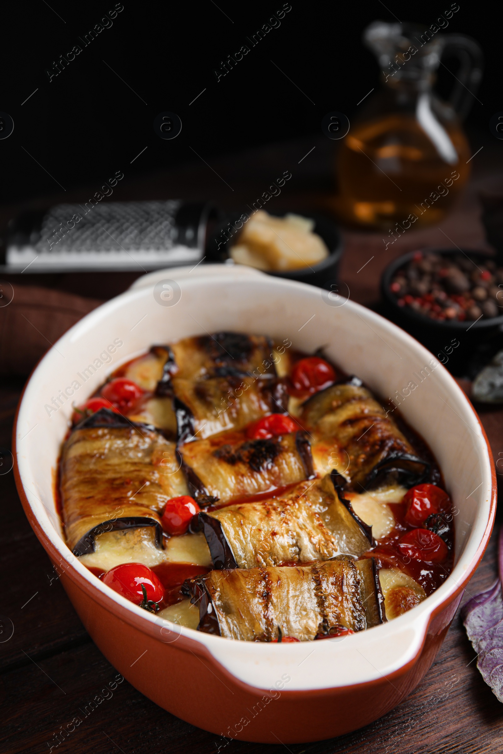 Photo of Tasty eggplant rolls with tomatoes and cheese in baking dish on wooden table