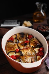 Tasty eggplant rolls with tomatoes and cheese in baking dish on wooden table