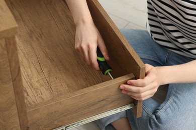Photo of Woman with screwdriver assembling drawer indoors, closeup