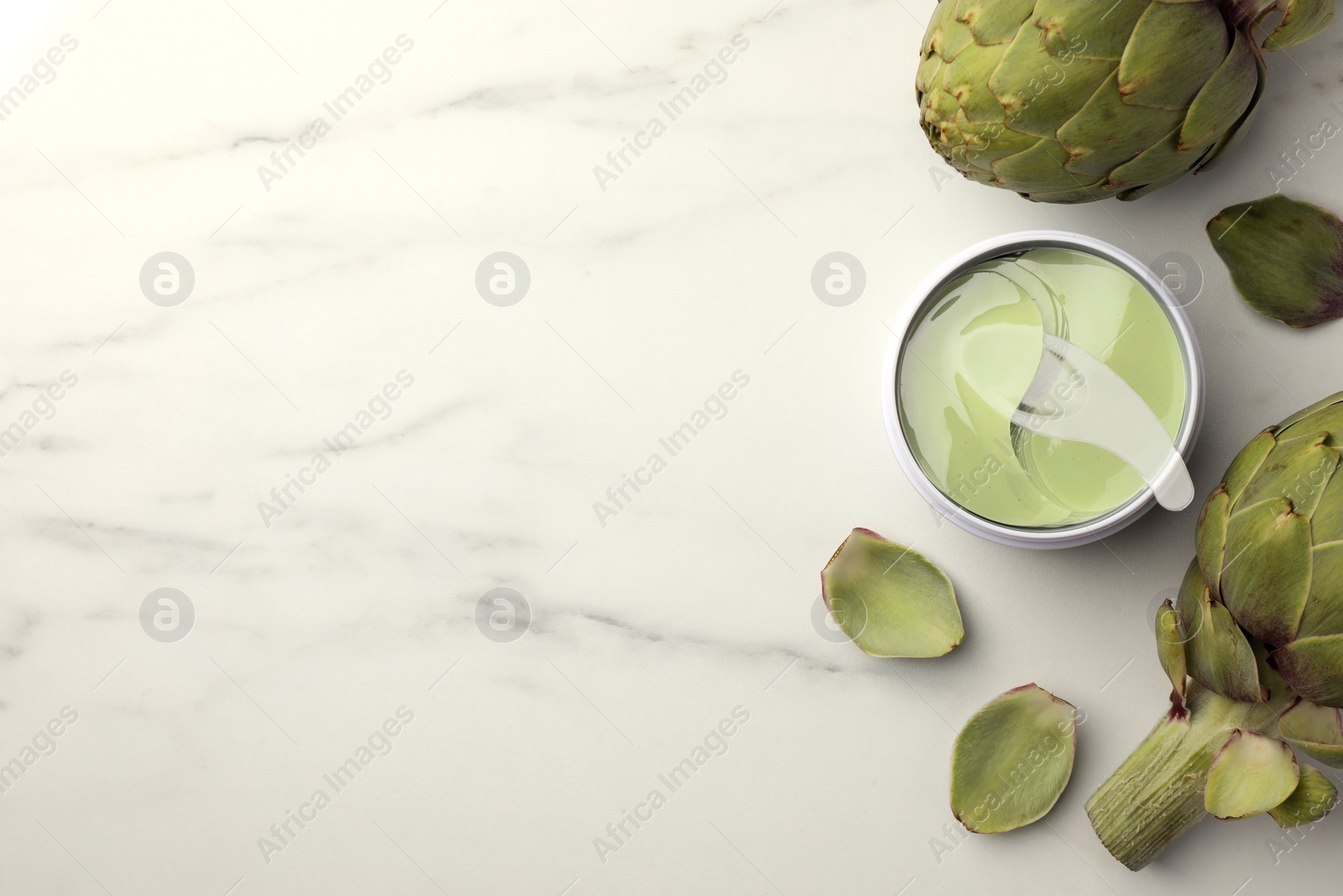 Photo of Package of under eye patches and artichokes on white marble table, flat lay with space for text. Cosmetic product
