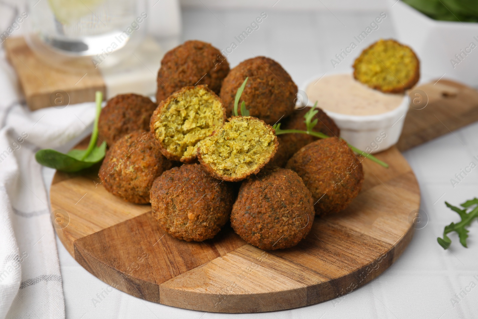 Photo of Delicious falafel balls, herbs and sauce on white tiled table