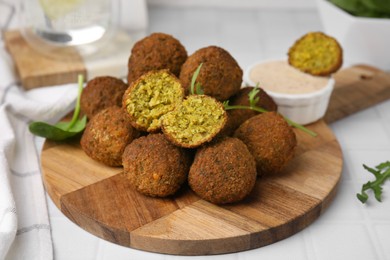 Delicious falafel balls, herbs and sauce on white tiled table