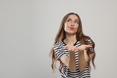 Photo of Beautiful young woman blowing kiss on light grey background, space for text