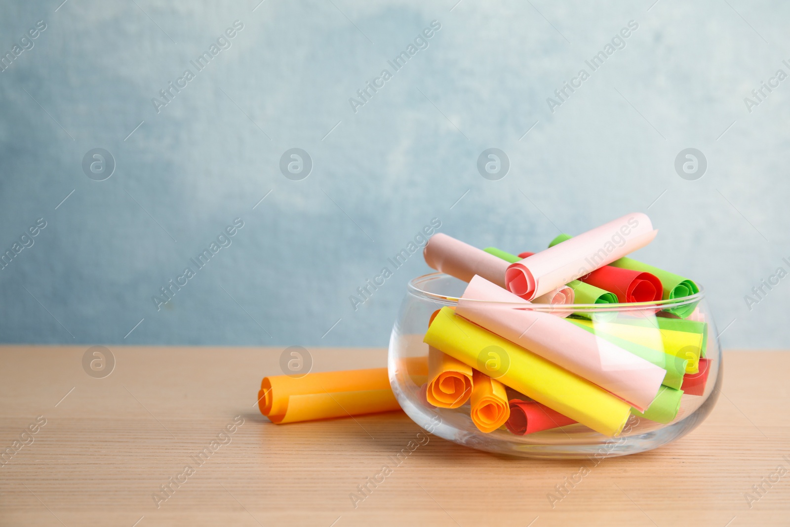 Photo of Colorful paper pieces for lottery in glass vase on wooden table. Space for text