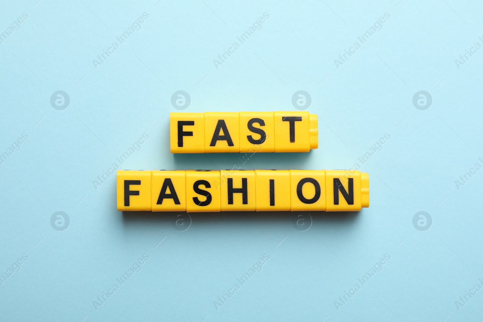 Photo of Yellow plastic cubes with phrase Fast Fashion on light blue background, flat lay