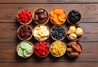 Photo of Bowls with different dried fruits on wooden background, flat lay. Healthy lifestyle