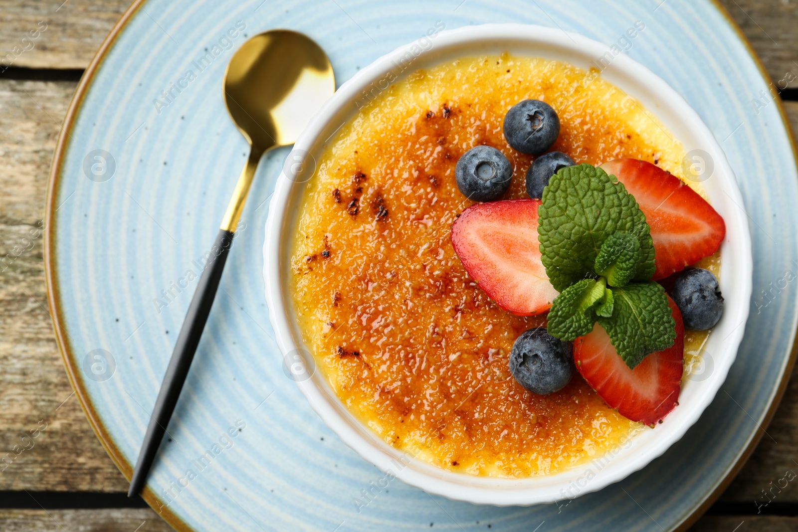 Photo of Delicious creme brulee with berries and mint in bowl on wooden table, top view