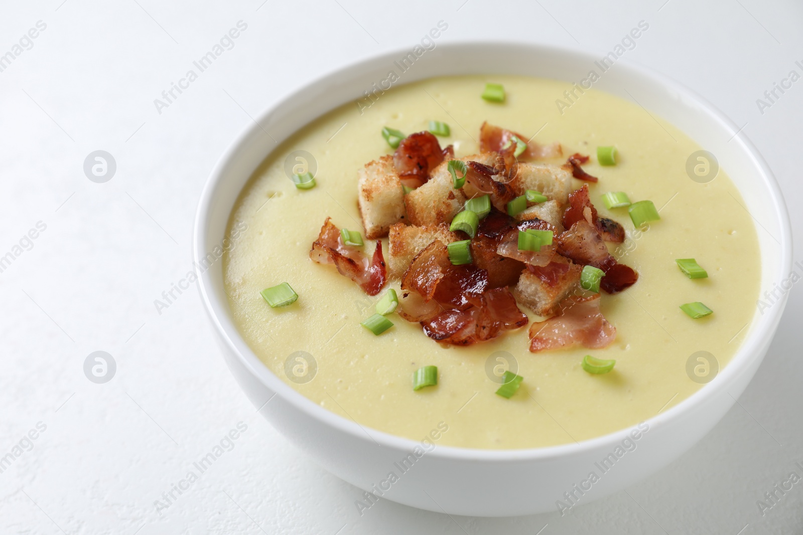 Photo of Tasty potato soup with bacon, green onion and croutons in bowl on white table, closeup