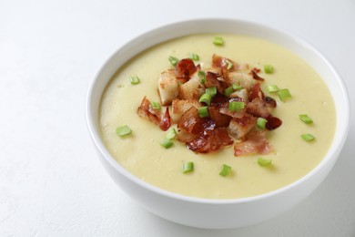 Photo of Tasty potato soup with bacon, green onion and croutons in bowl on white table, closeup