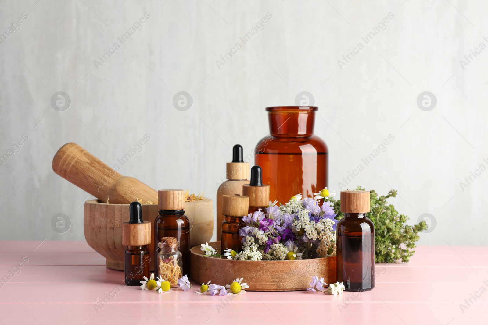 Photo of Aromatherapy. Different essential oils, mortar, pestle and flowers on pink wooden table