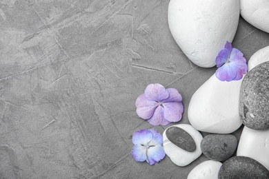 Zen stones and exotic flowers on grey background, top view with space for text