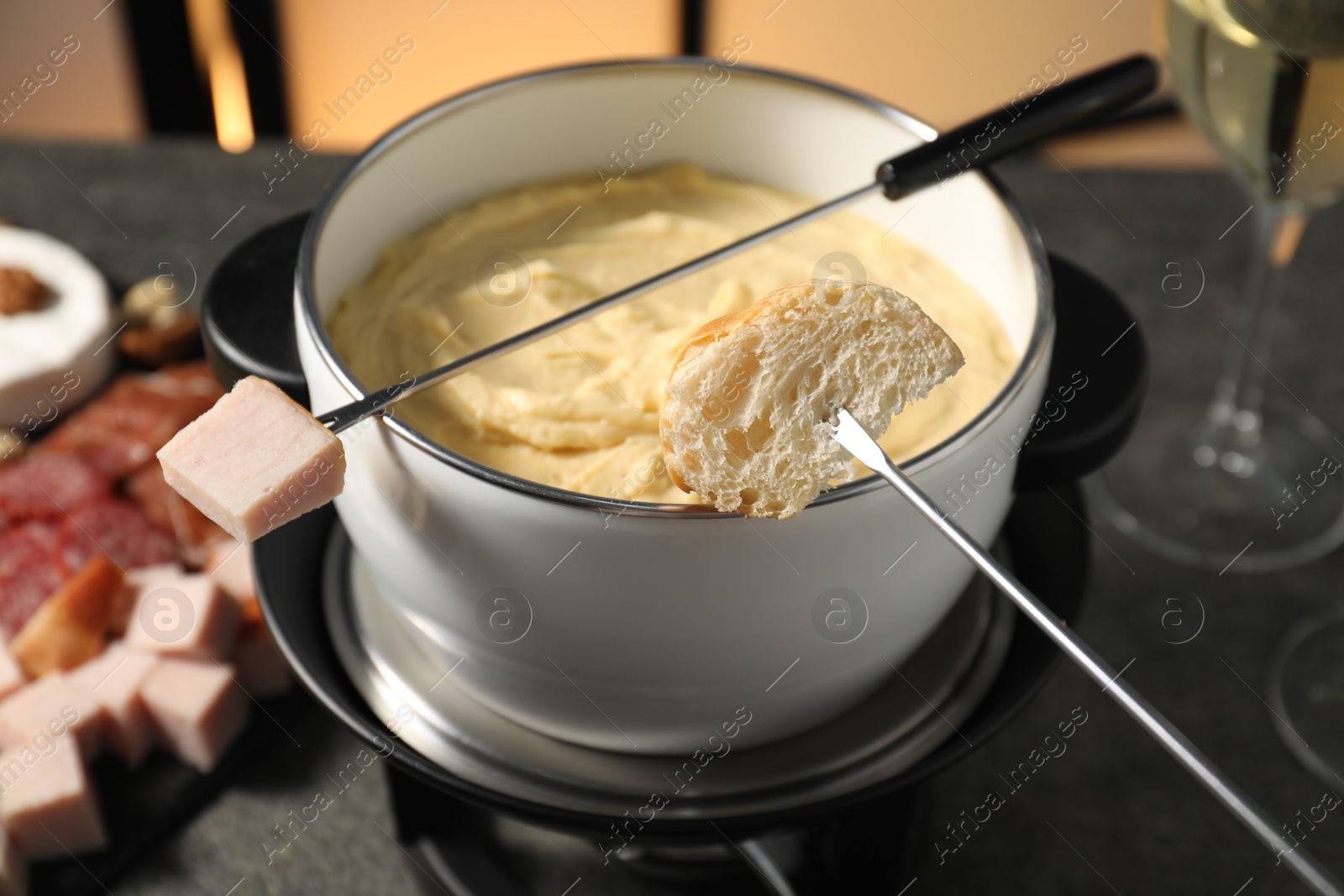 Photo of Forks with pieces of ham, bread and fondue pot with melted cheese on grey table, closeup