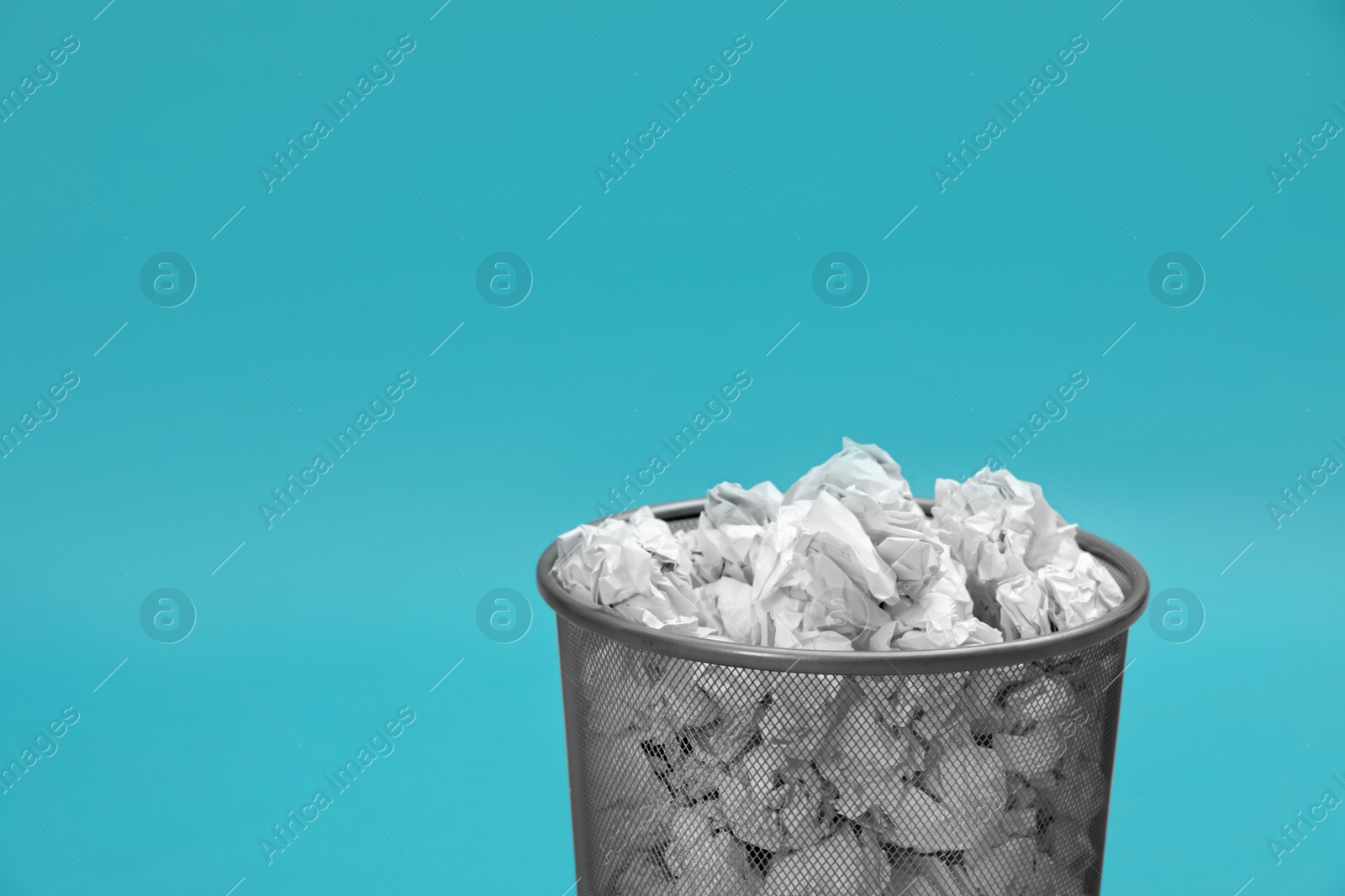 Photo of Metal bin with crumpled paper on color background, space for text