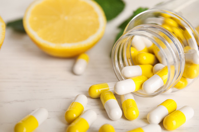 Bottle with vitamin pills and lemon on light table, closeup