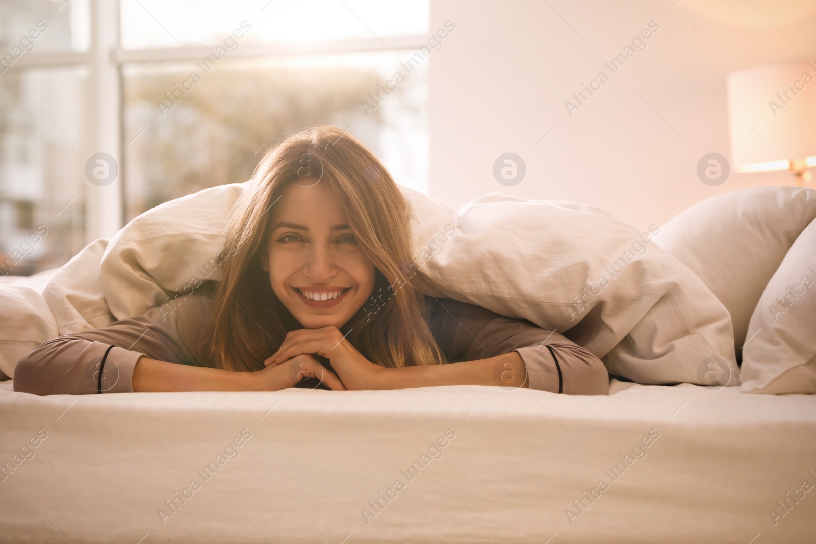 Photo of Cheerful woman covered with warm white blanket lying in bed indoors