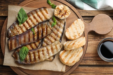 Delicious grilled eggplant slices served on wooden table, flat lay