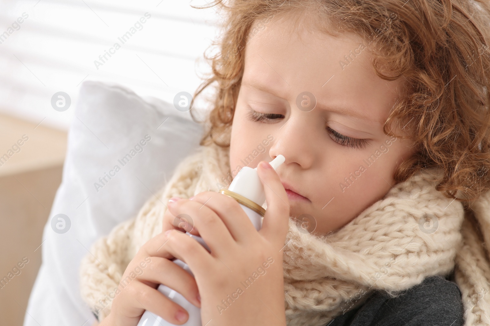 Photo of Cute little boy using nasal spray on bed indoors, closeup