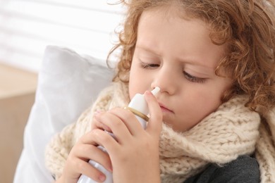 Cute little boy using nasal spray on bed indoors, closeup