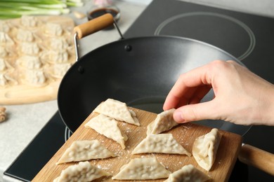 Photo of Woman putting raw gyoza on frying pan with hot oil, closeup