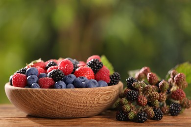 Photo of Bowl with different fresh berries on wooden table outdoors