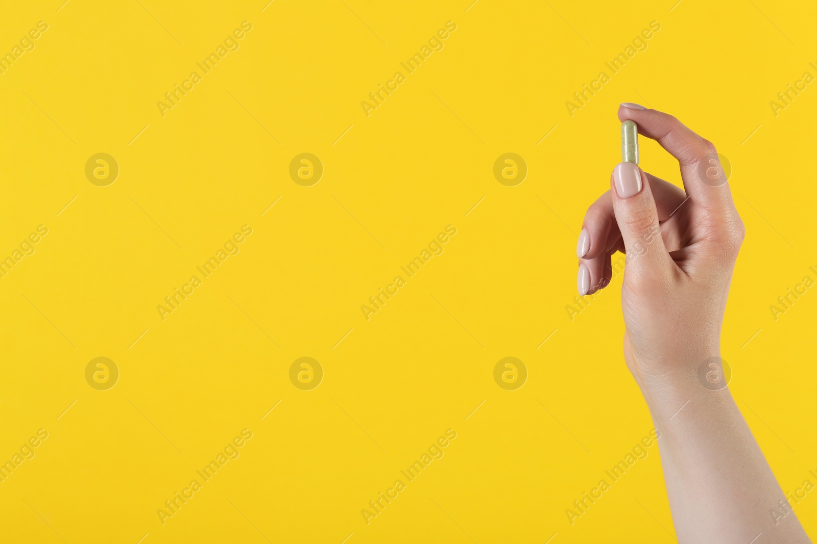 Photo of Woman holding vitamin capsule on yellow background, closeup with space for text. Health supplement