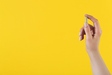 Woman holding vitamin capsule on yellow background, closeup with space for text. Health supplement