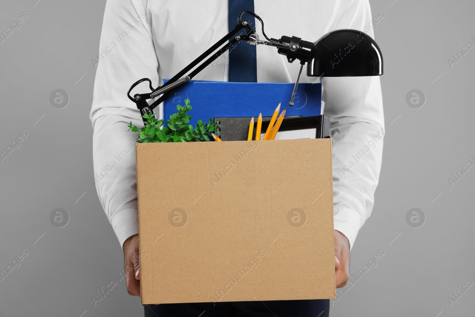 Photo of Unemployed man with box of personal office belongings on light grey background, closeup