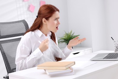 Woman popping bubble wrap at desk in office. Stress relief