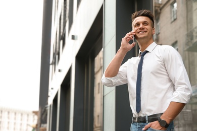 Portrait of handsome young man talking by phone on city street. Space for text