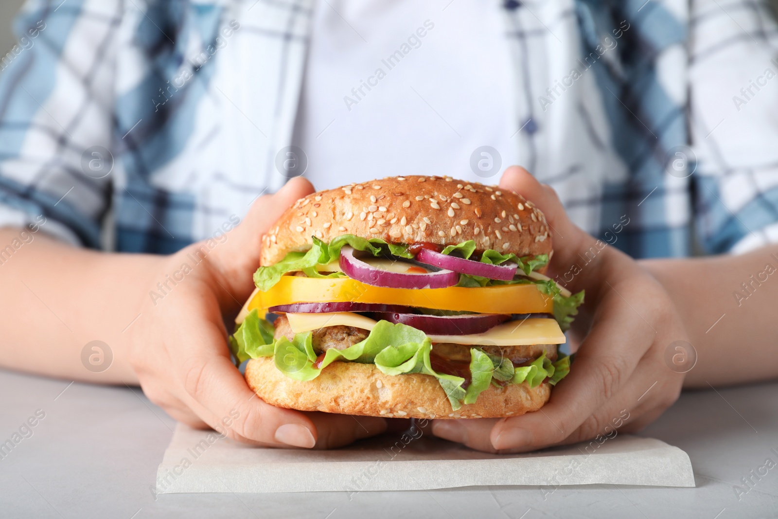 Photo of Woman with tasty hamburger at table, closeup