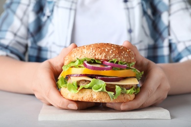 Photo of Woman with tasty hamburger at table, closeup