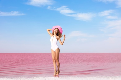 Photo of Beautiful woman in swimsuit posing near pink lake on sunny day