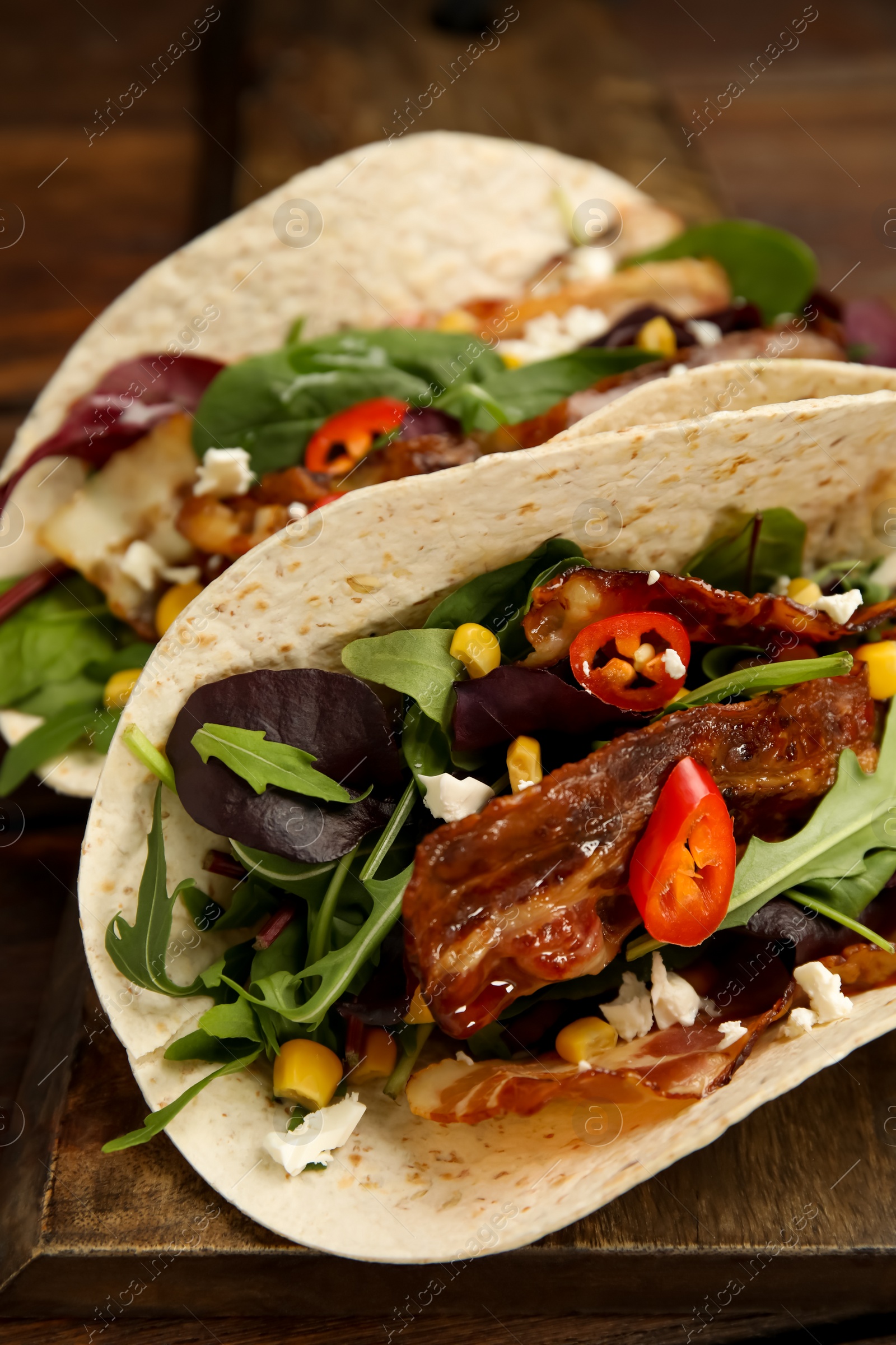 Photo of Delicious tacos with fried bacon, vegetables and cheese on wooden board, closeup