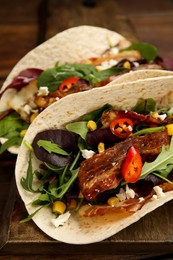 Photo of Delicious tacos with fried bacon, vegetables and cheese on wooden board, closeup