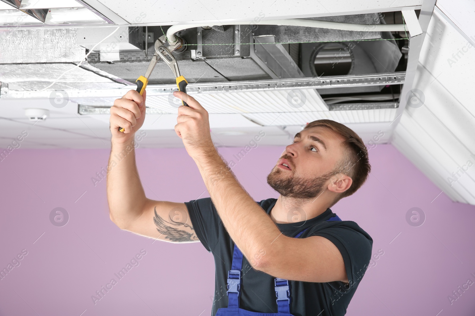 Photo of Young male technician repairing air conditioner indoors