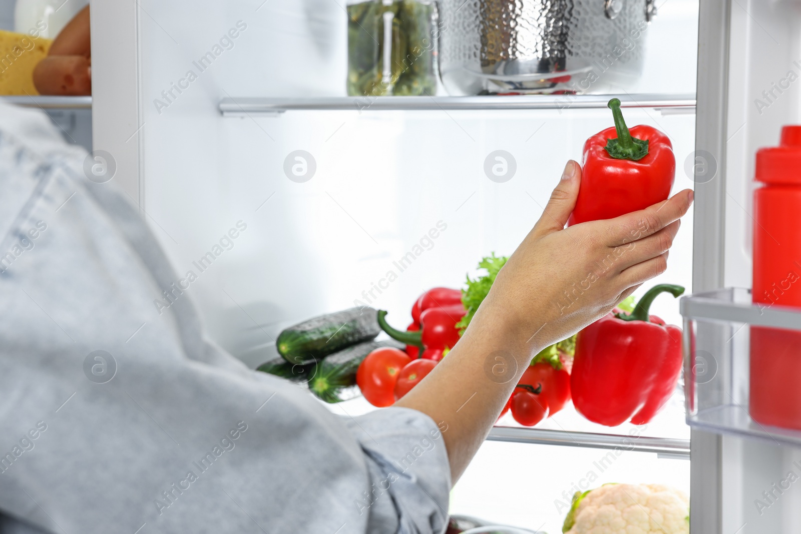 Photo of Young woman taking red bell pepper out of refrigerator, closeup