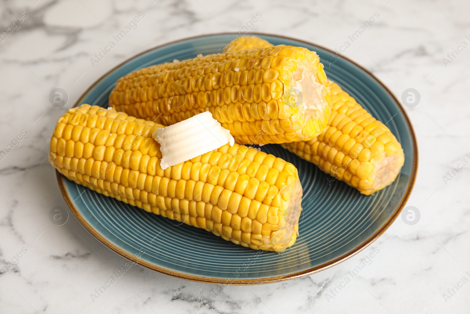 Photo of Delicious boiled corn with butter on white marble table