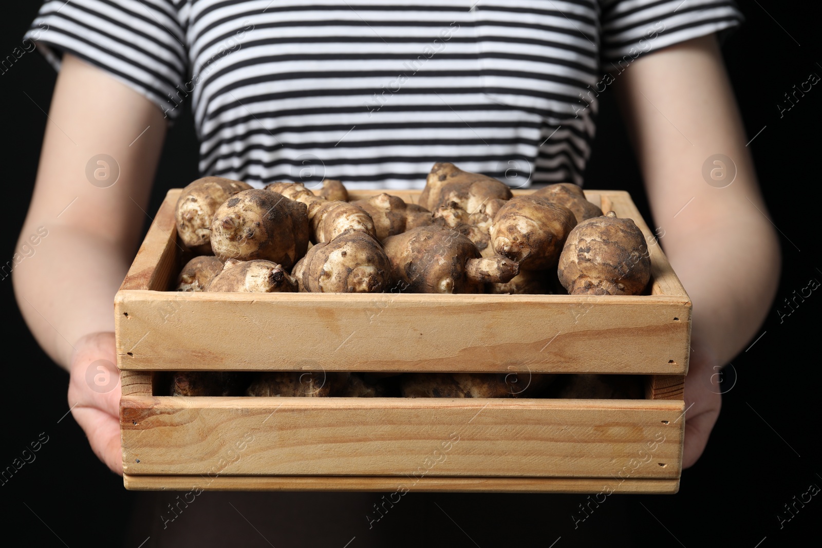 Photo of Woman holding wooden crate with Jerusalem artichokes on black background, closeup