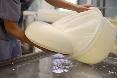 Photo of Worker taking fresh cheese from mould at modern factory, closeup