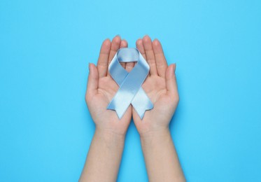 Photo of Woman holding light blue awareness ribbon on color background, top view