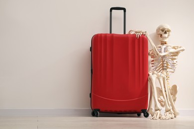 Photo of Waiting concept. Human skeleton with suitcase near light grey wall, space for text