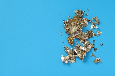 Photo of Pieces of edible gold leaf on light blue background, flat lay. Space for text