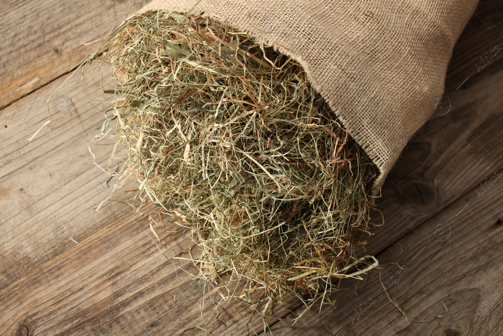 Photo of Burlap sack with dry herb on wooden table, top view