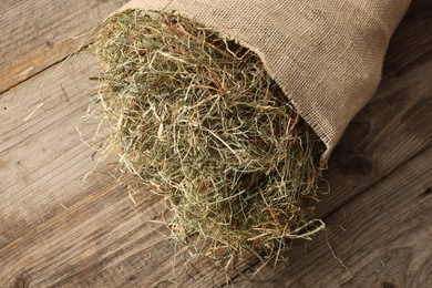 Photo of Burlap sack with dry herb on wooden table, top view