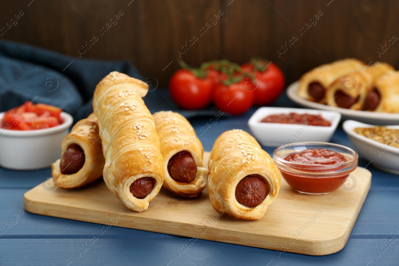 Photo of Delicious sausage rolls and ingredients on blue wooden table