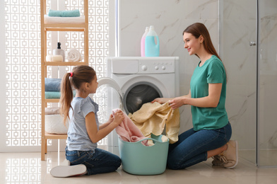 Photo of Mother and little daughter with clean laundry in bathroom